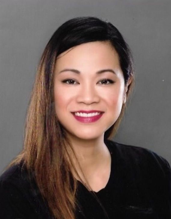 Portrait of a woman with long hair, smiling against a gray background.